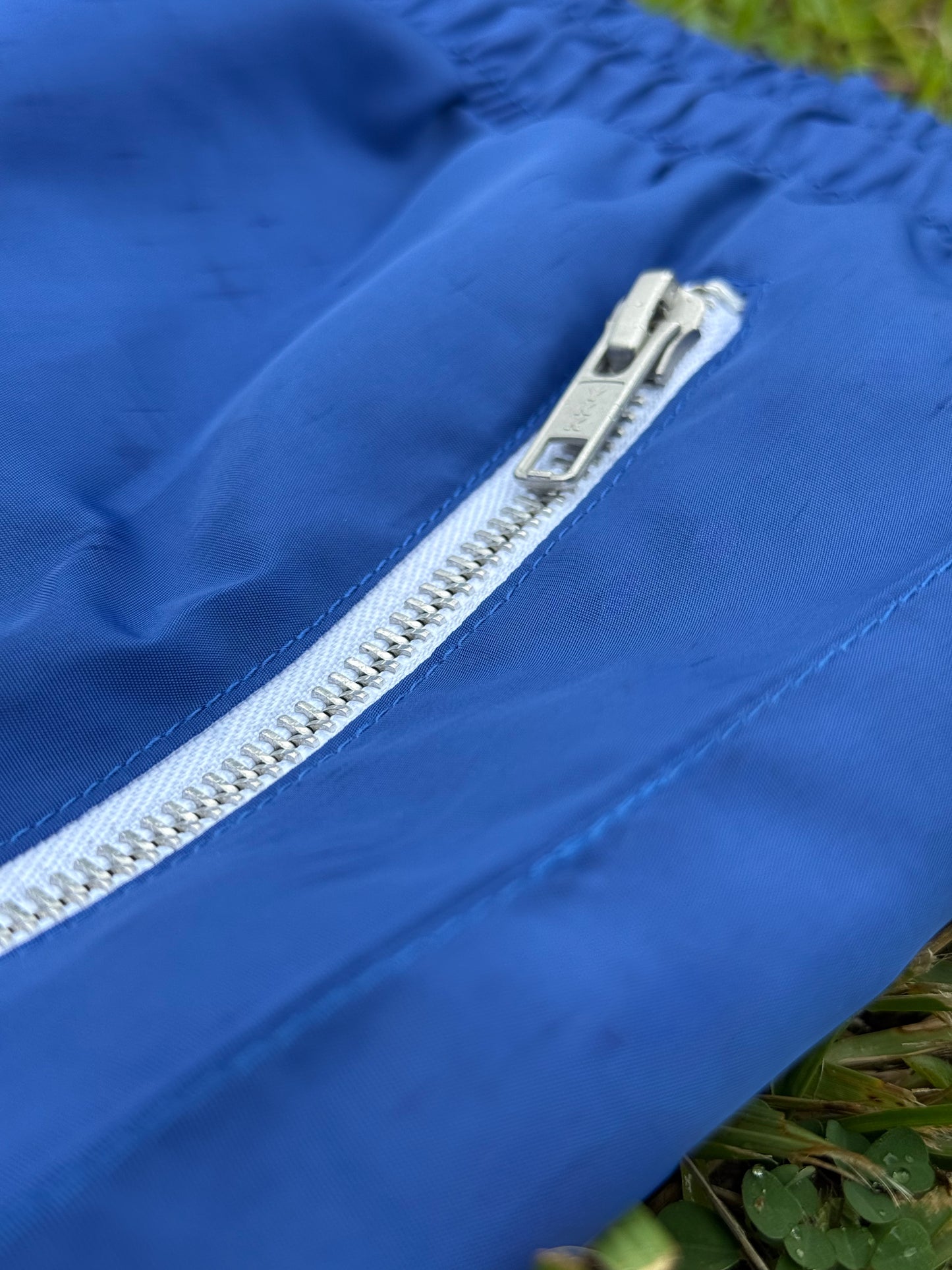 Close-up of a blue jacket with a white zipper on grass.